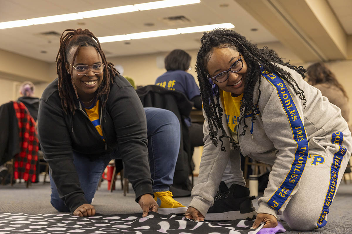 Two UM-Flint volunteers smiling while working on a blanket.