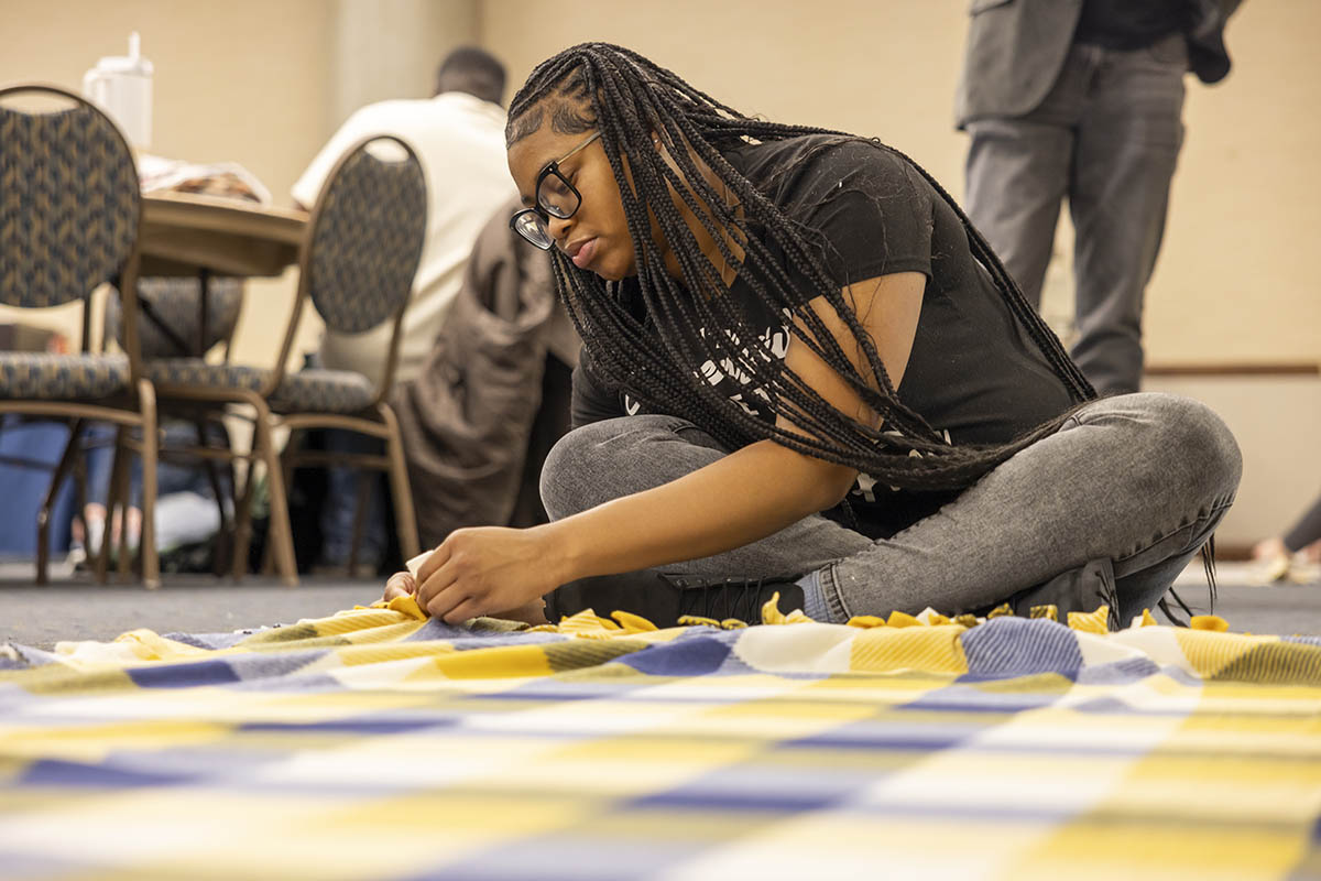 A UM-Flint volunteer seated on the floor tying a blanket.