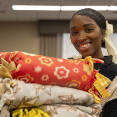 A UM-Flint staff member smiling while holding a stack of blankets made during MLK Day.