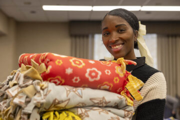 A UM-Flint staff member smiling while holding a stack of blankets made during MLK Day.