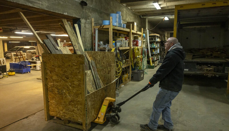 A UM-Flint volunteer moving building materials in a workshop with a dolly