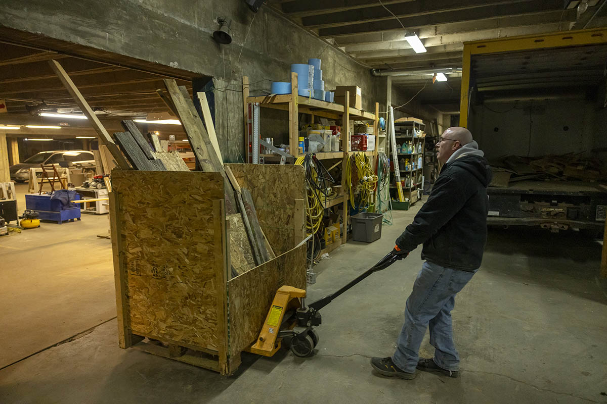 A UM-Flint volunteer moving building materials in a workshop with a dolly