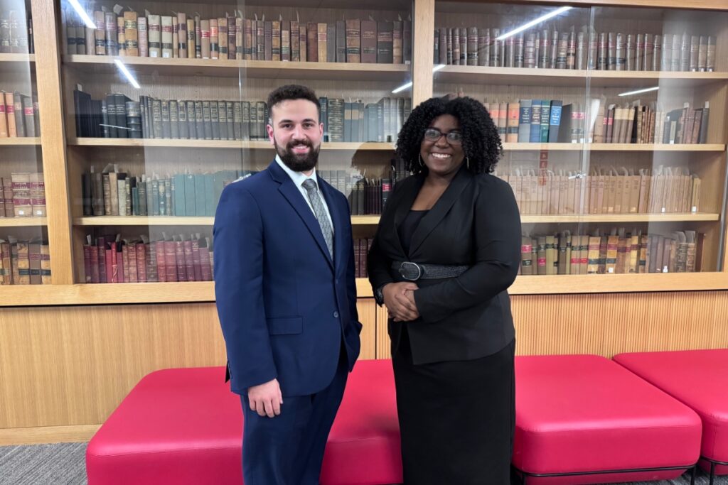 A man and woman posing in front of a bookshelf smiling for the camera