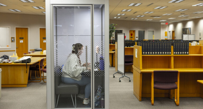 A student working on her laptop inside a quiet study pod in the library.