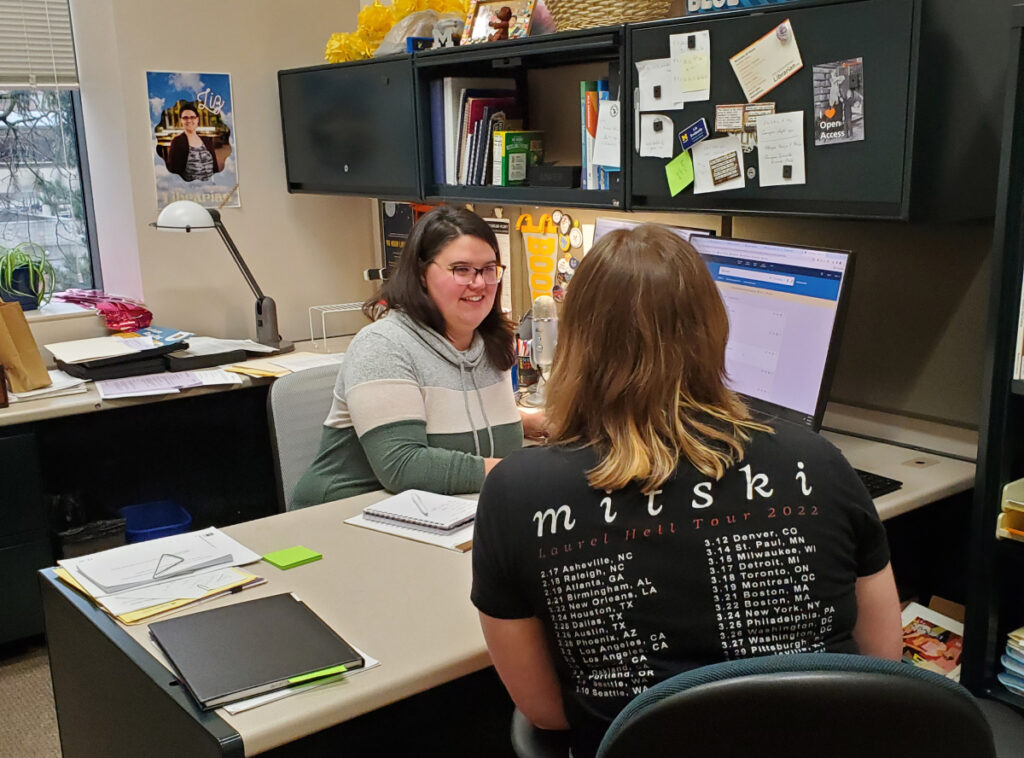 Liz Svoboda behind her desk with a student seated across from her.