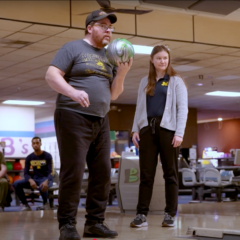 An occupational therapy patient getting ready to throw a bowling ball down the lane at an alley while an OT student stands behind him.