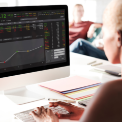A woman sitting at a desktop computer looking at a graph of stock performance