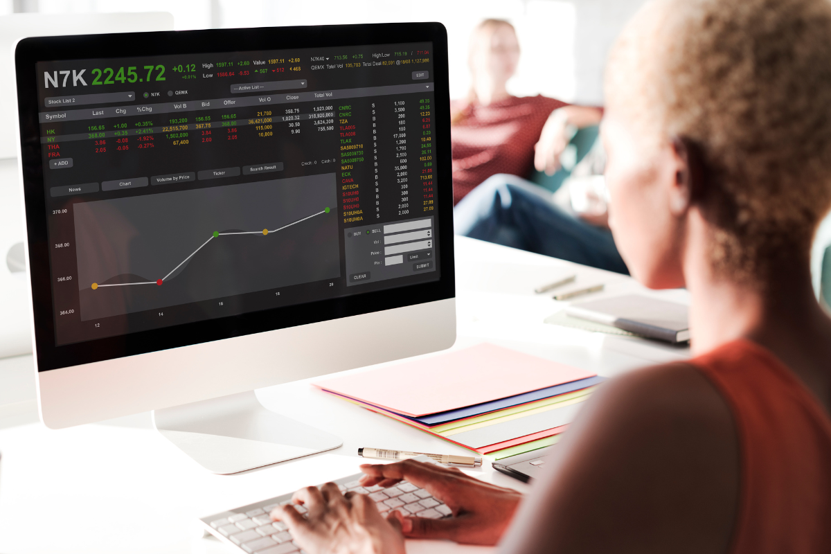 A woman sitting at a desktop computer looking at a graph of stock performance