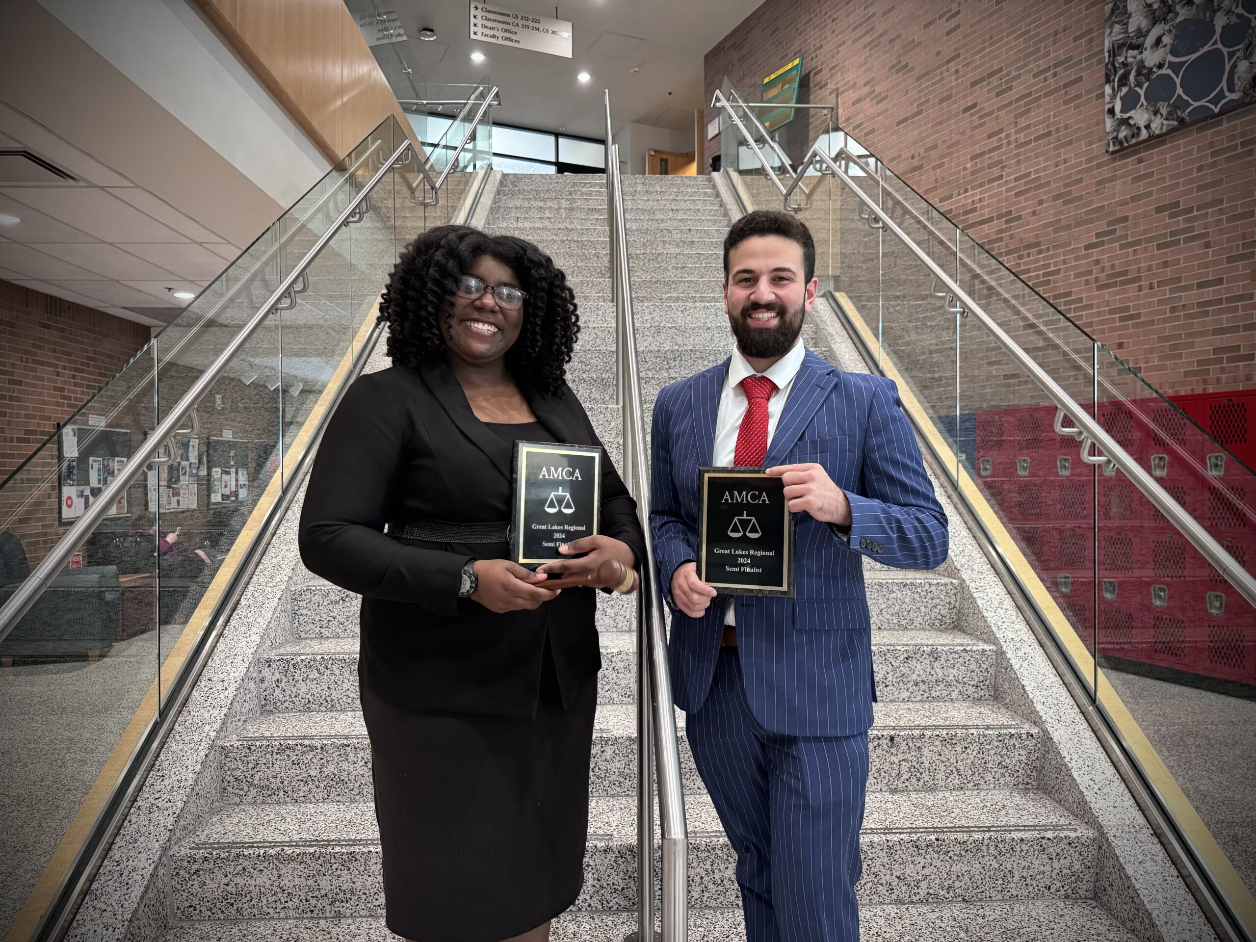 A man and woman in professional attire posing in front of a staircase.