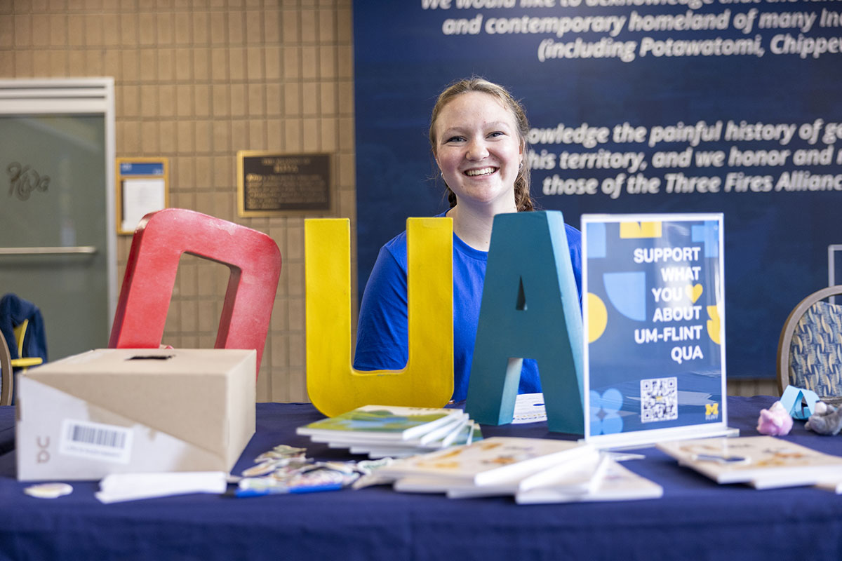 A student sitting behind a table with "QUA" block letters.