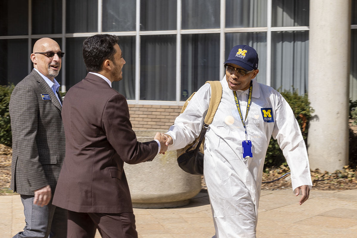 Chancellor Alexander in a white protective suit shaking hands with a student before behind duct taped.