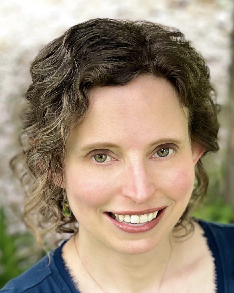 A portrait of a white woman with curly brown hair smiling at the camera