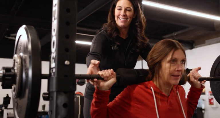 Amber Schlemmer spotting a patient while the patient performs a back squat with a barbell