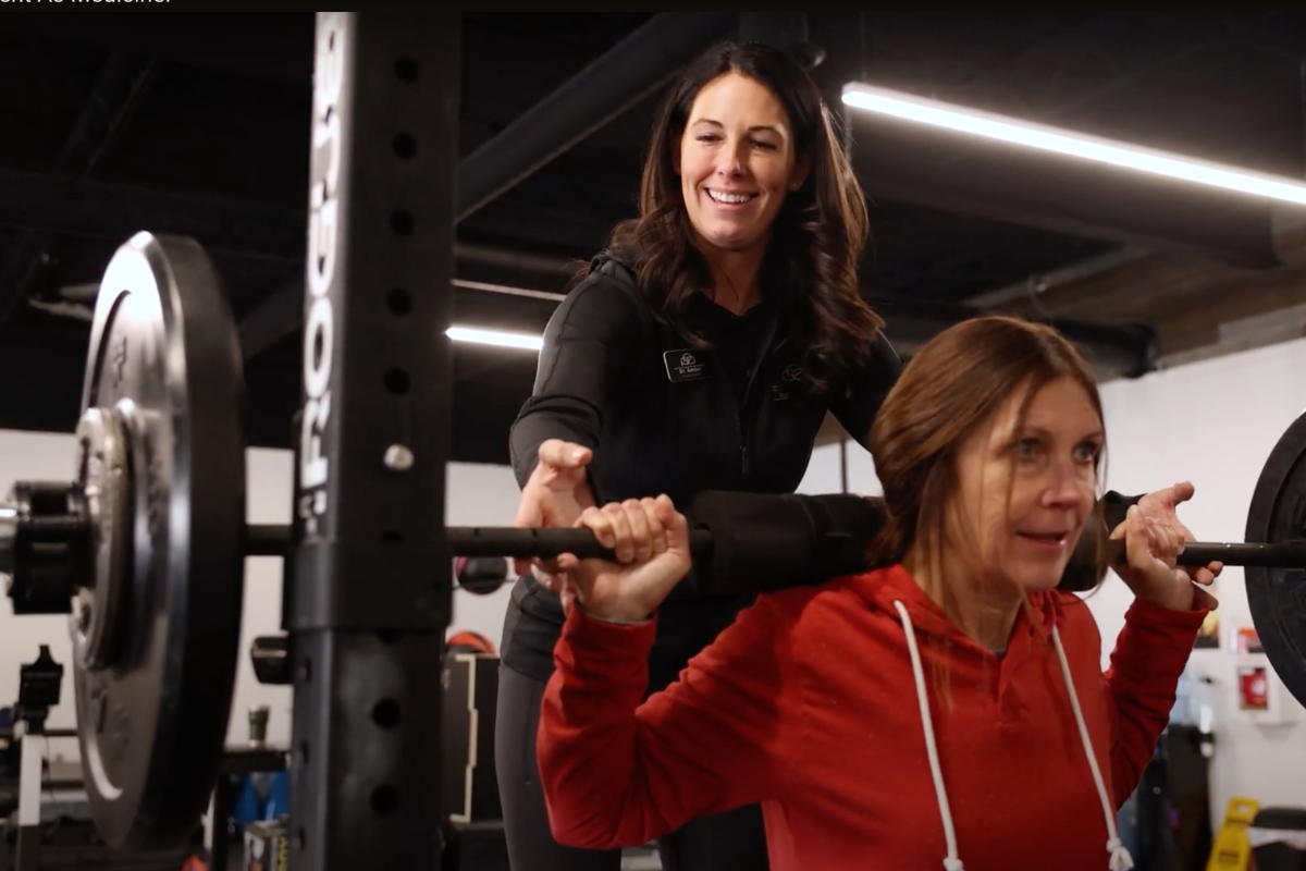 Amber Schlemmer spotting a patient while the patient performs a back squat with a barbell