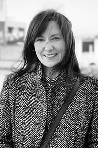 A black and white portrait of Erin Evans-Leonard, a white woman with long dark hair wearing a black and whit houndstooth coat