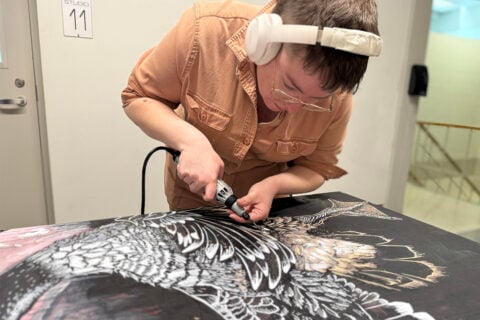 A woman is wearing white headphones and using an engraving on a large wooden stamp