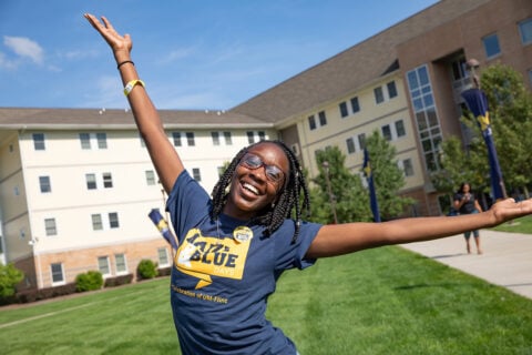 A student celebrating with her arms outstretched on the lawn outside of First Street Residence Hall.