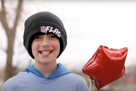 A boy smiling for the camera holding a red balloon