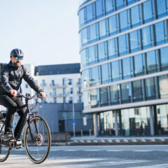 A male bicycle courier with sunglasses cycling through a city, delivering packages.