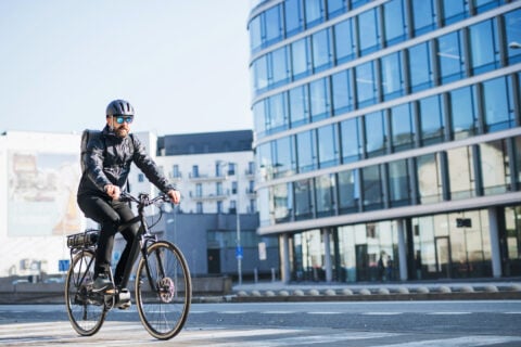 A male bicycle courier with sunglasses cycling through a city, delivering packages.