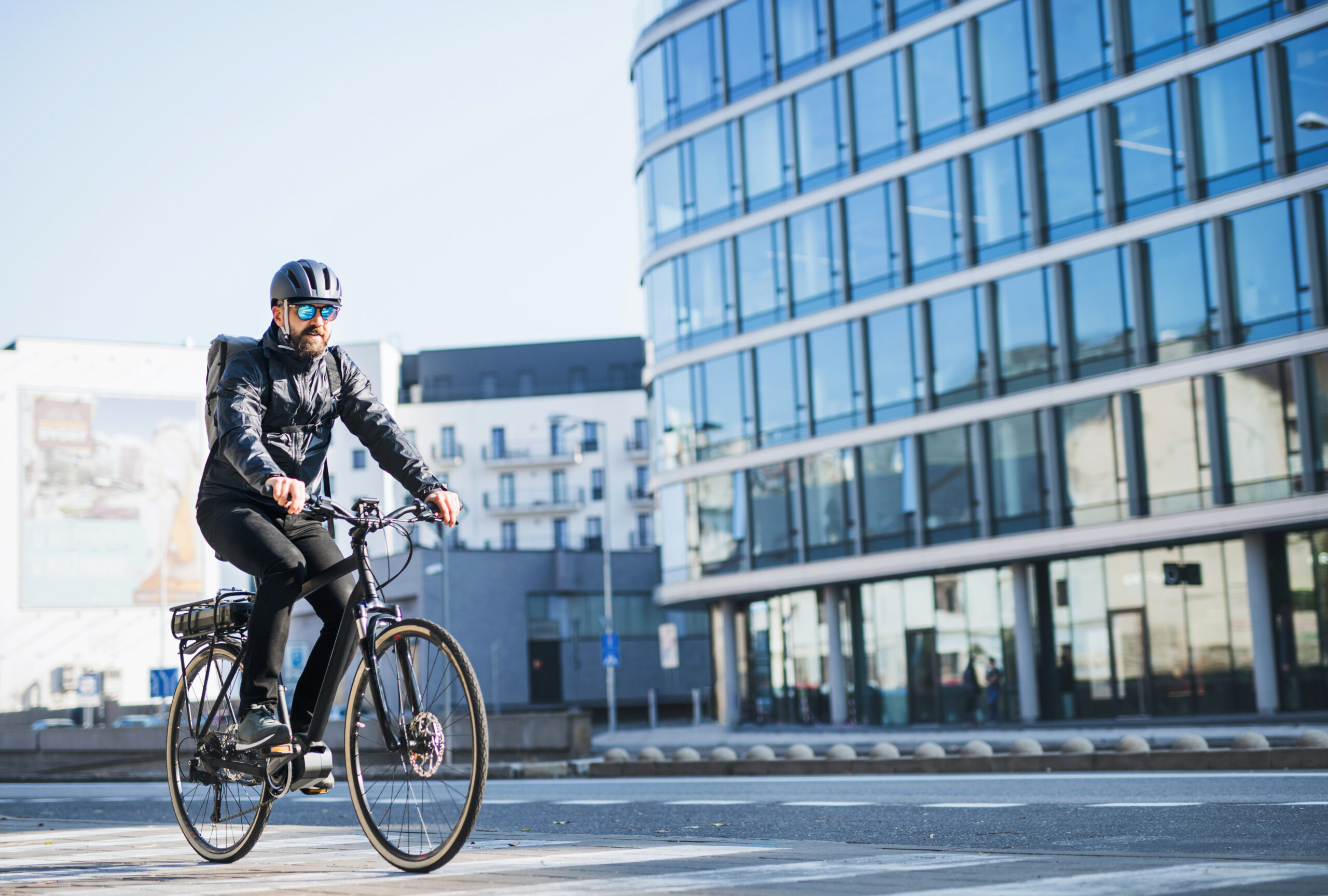 A male bicycle courier with sunglasses cycling through a city, delivering packages.