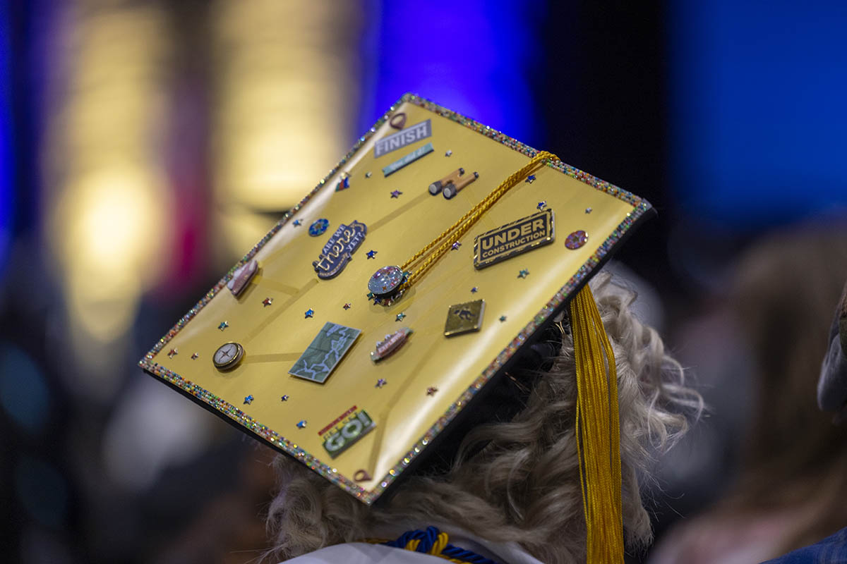 A decorated graduation cap with pins that say "under construction" etc.