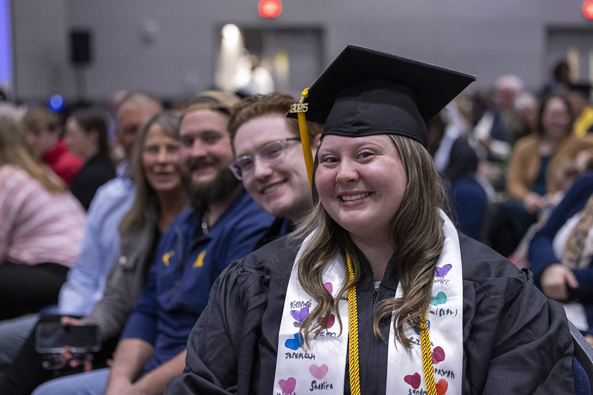 A graduating student smiling for the camera in the crowd with her family in the background.