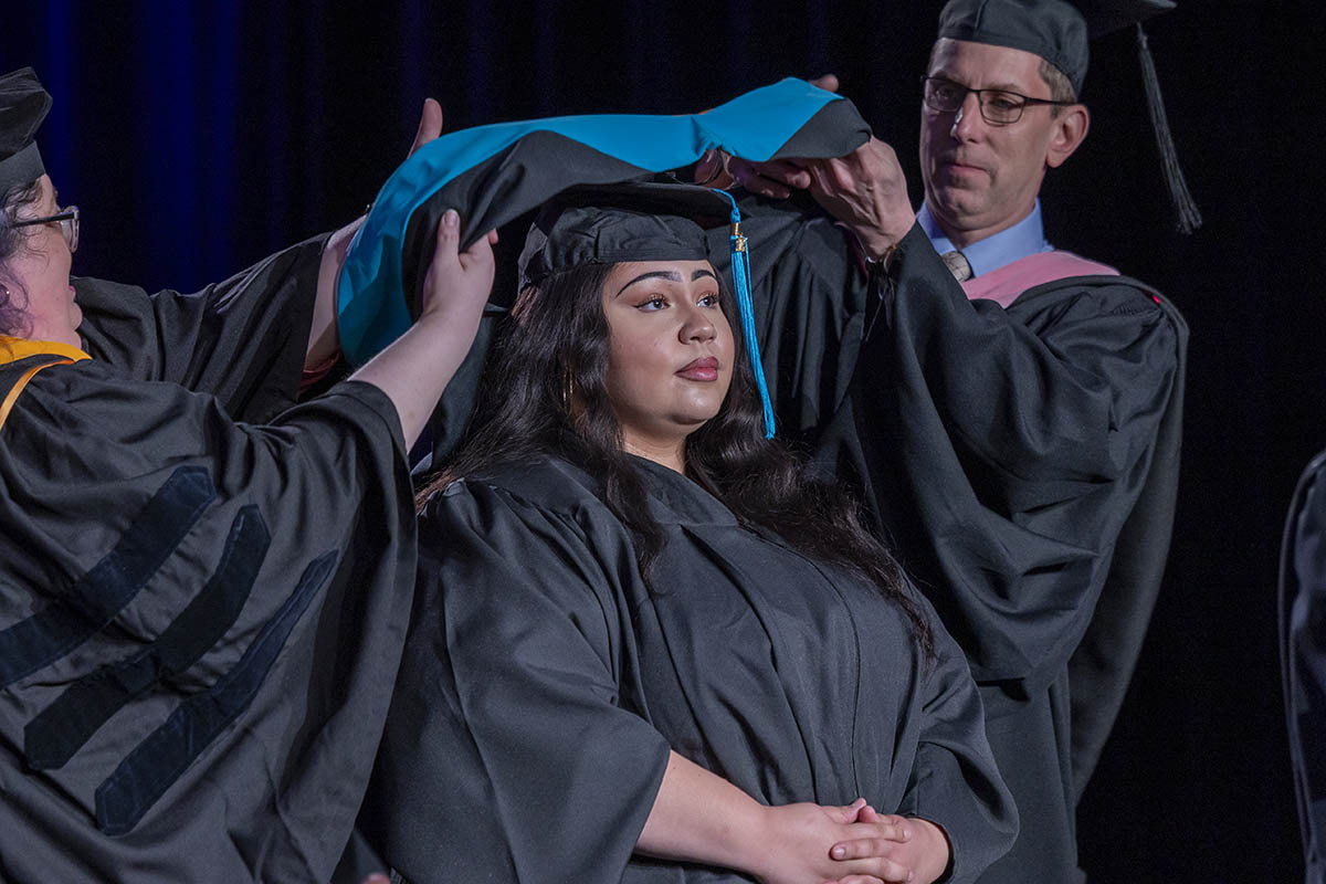 A student being arrayed in her graduate hood on stage.