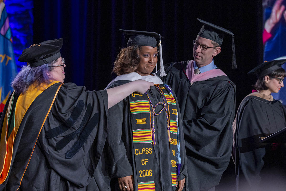 A student being arrayed in her graduate hood on stage.