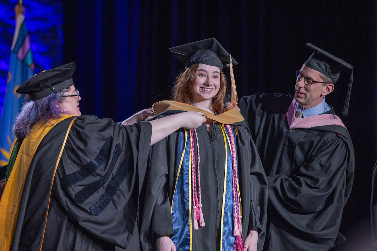 A student being arrayed in her graduate hood on stage.