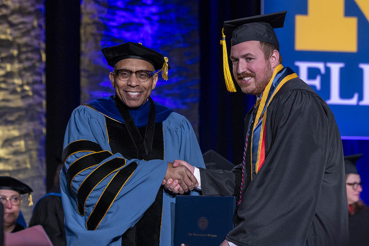 A student receiving his diploma cover from Chancellor Laurence Aleander on stage.