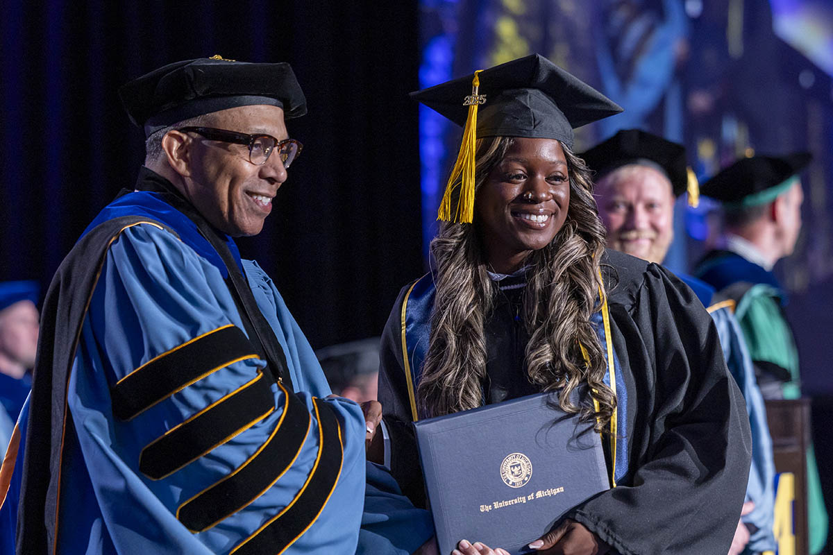 A student receiving her diploma cover from Chancellor Laurence Aleander on stage.
