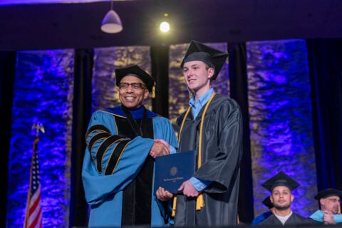 Chancellor Laurence Alexander shakes hands with a School of Nursing student on stage with the photo subjects in graduation regalia.