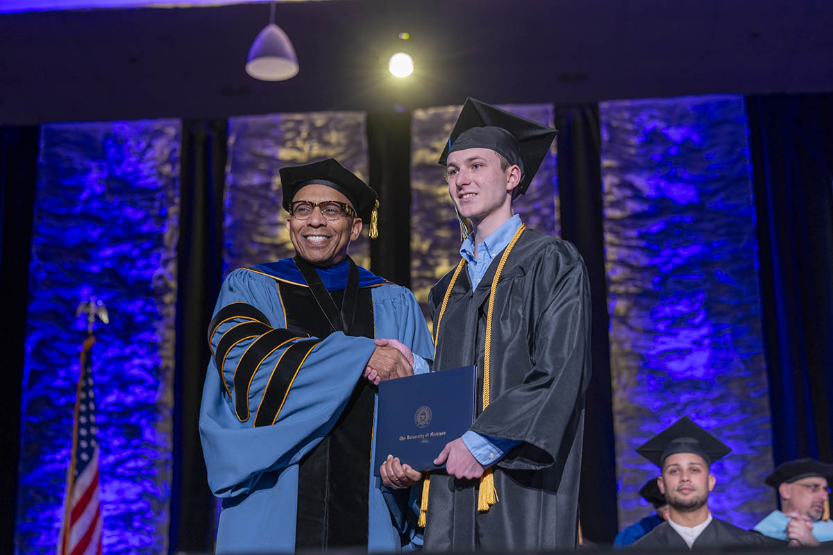 Chancellor Laurence Alexander shakes hands with a School of Nursing student on stage with the photo subjects in graduation regalia.