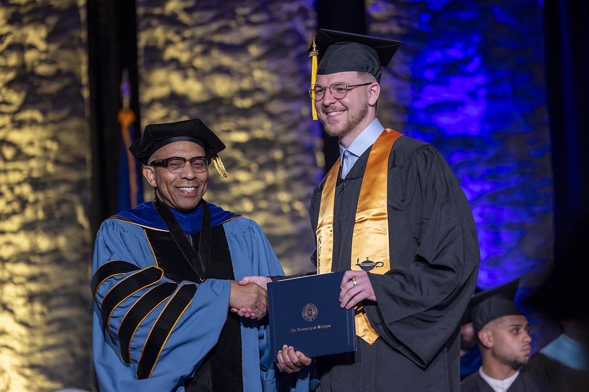 A student shaking hands with Chancellor Alexander receiving his diploma on stage.