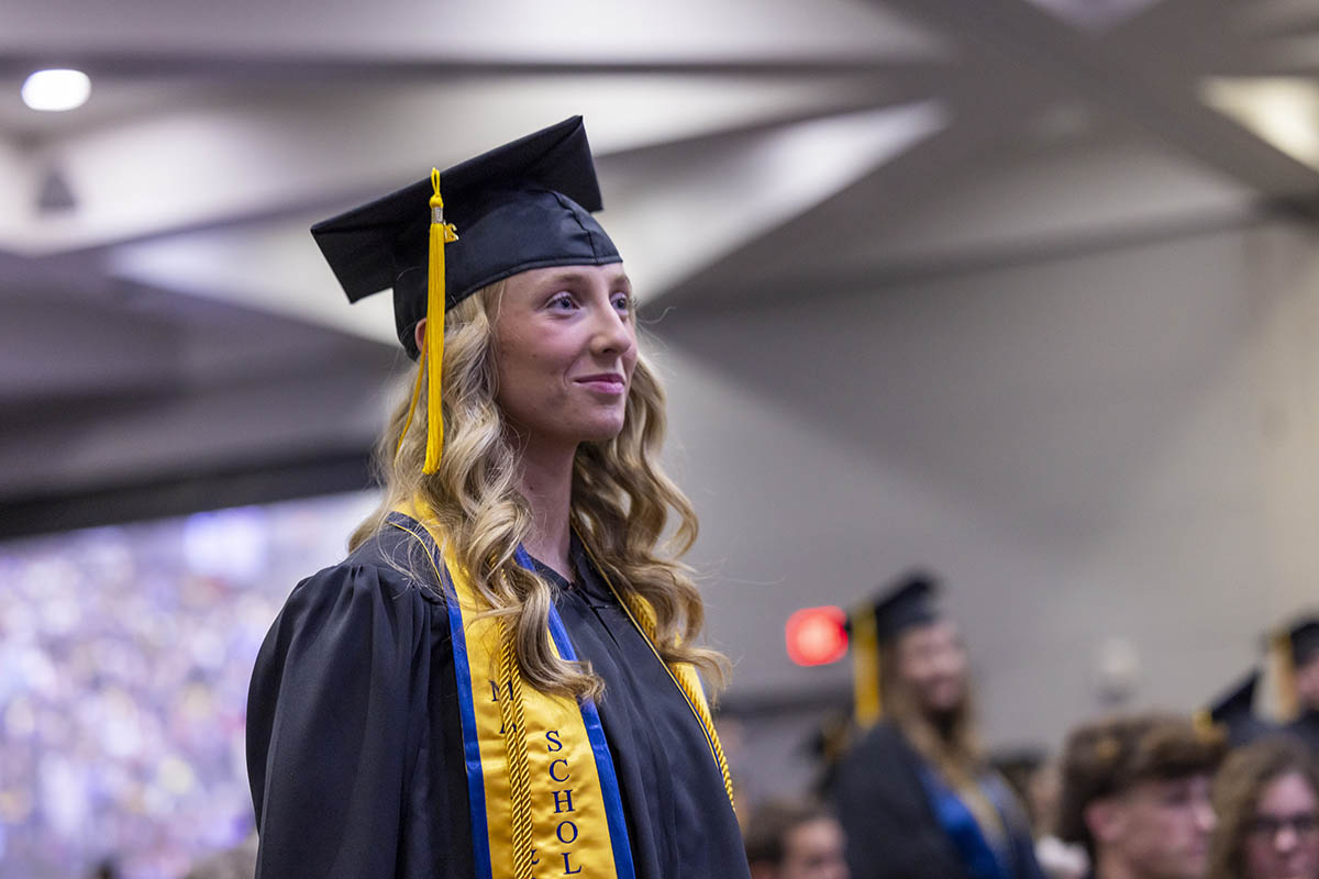 A graduating student standing in the crowd being recognized for graduating with honors