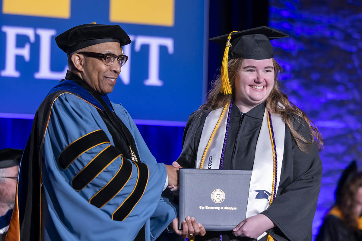A student receiving her diploma on stage from Chancellor Laurence Alexander.