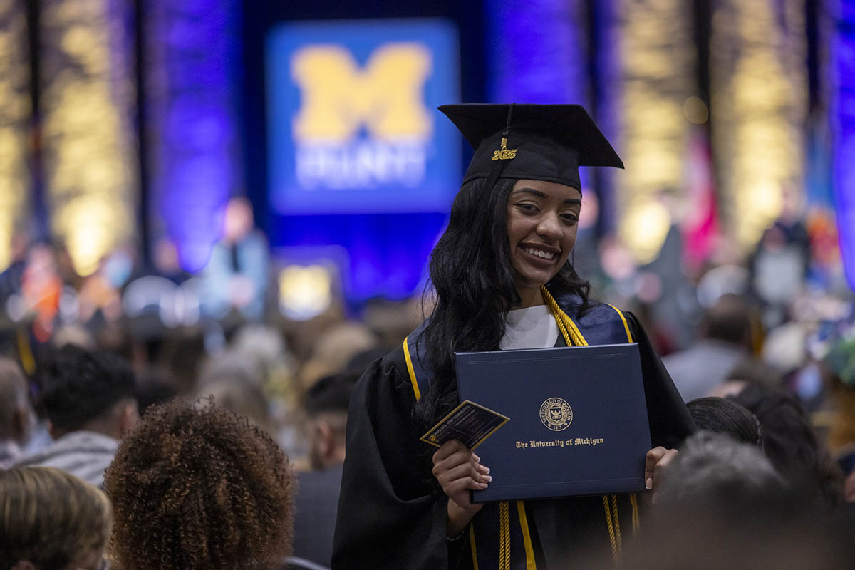 A student standing in the crowd posing with her diploma cover for the camera