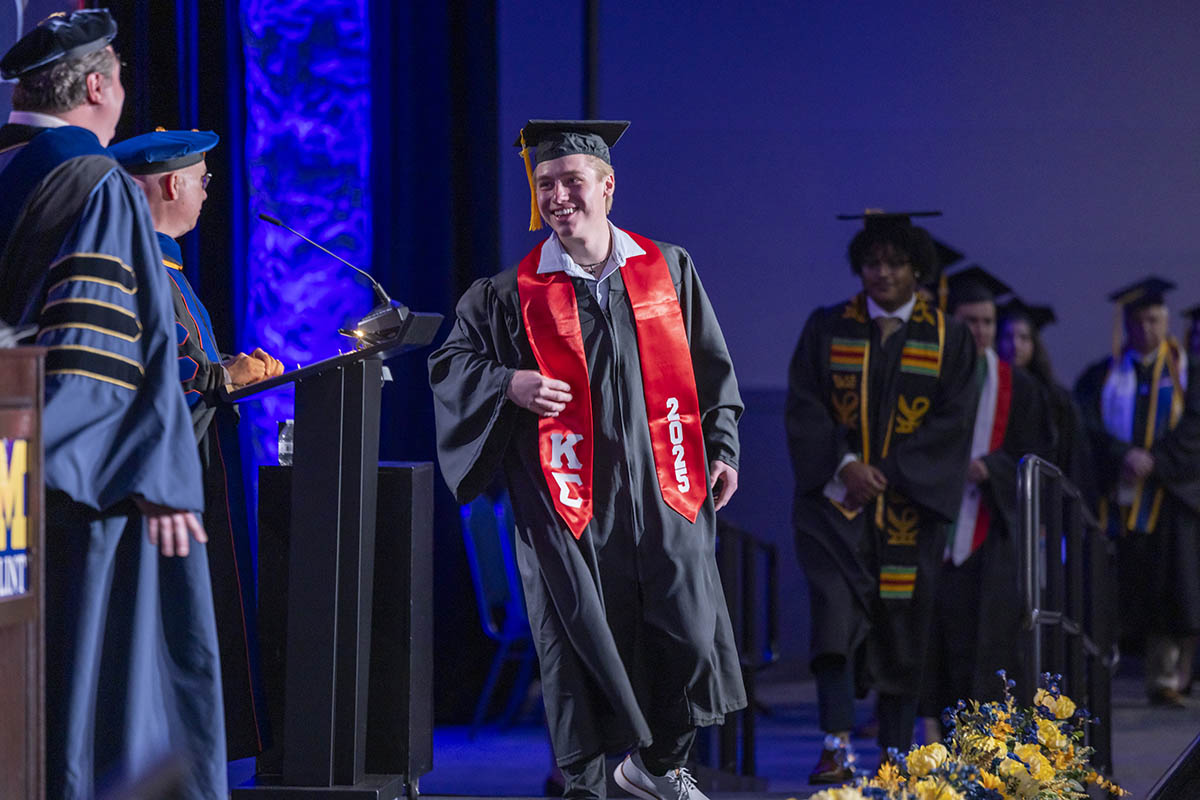 A graduating student in a Kappa Sigma stole walking across the stage.