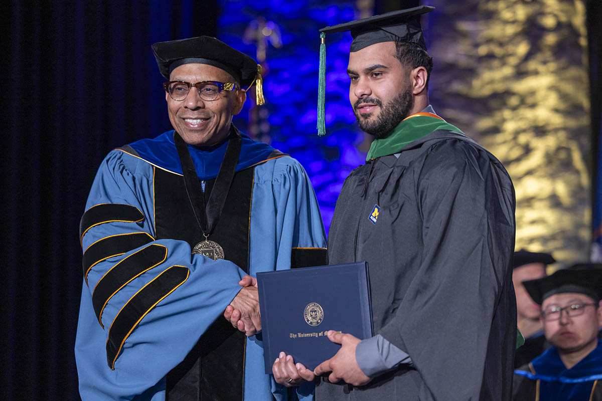 A student receiving his diploma on stage from Chancellor Laurence Alexander.