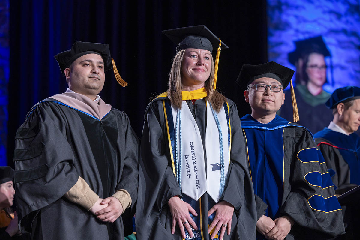 A student standing on stage with two faculty members