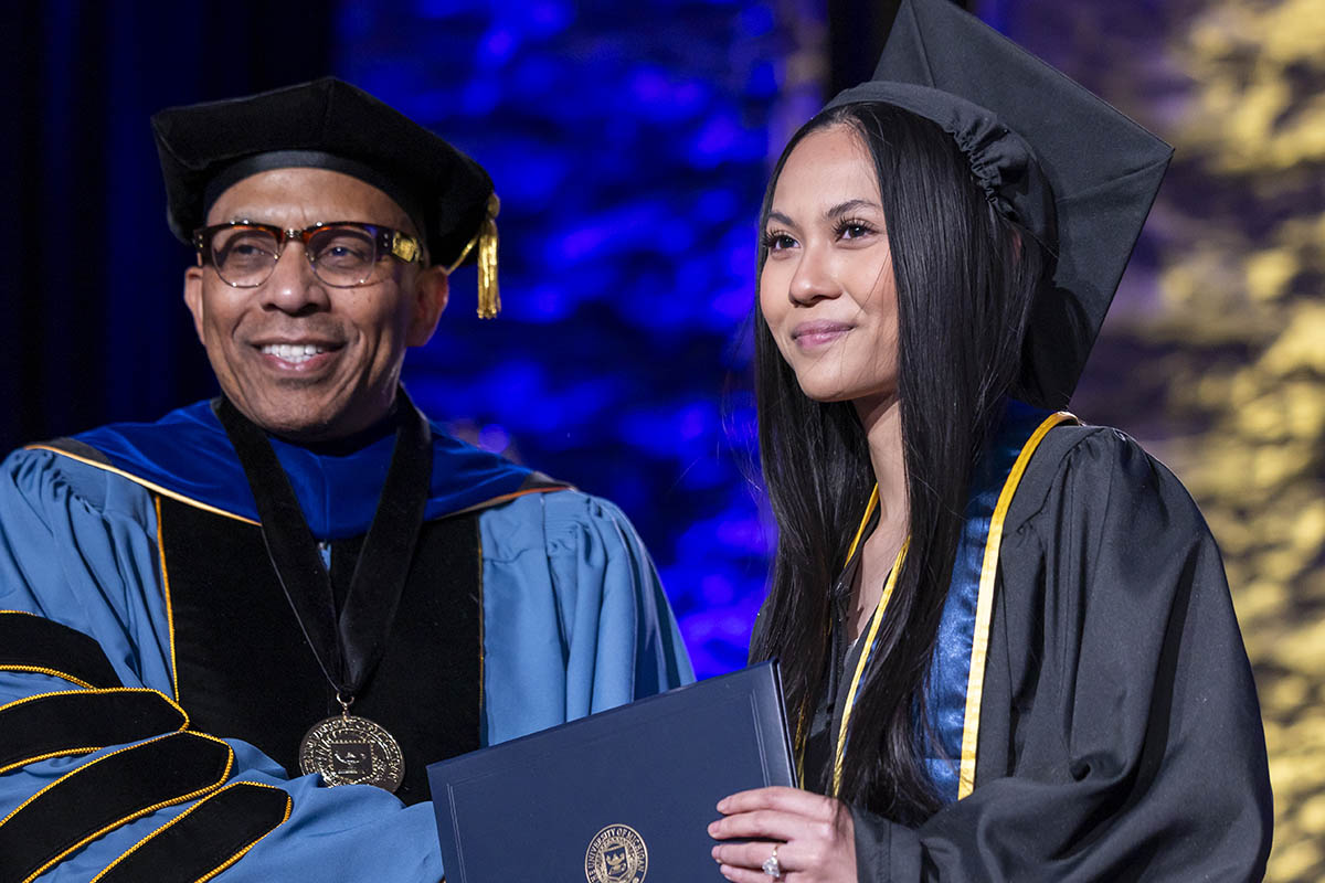 A student receiving her diploma on stage from Chancellor Laurence Alexander.