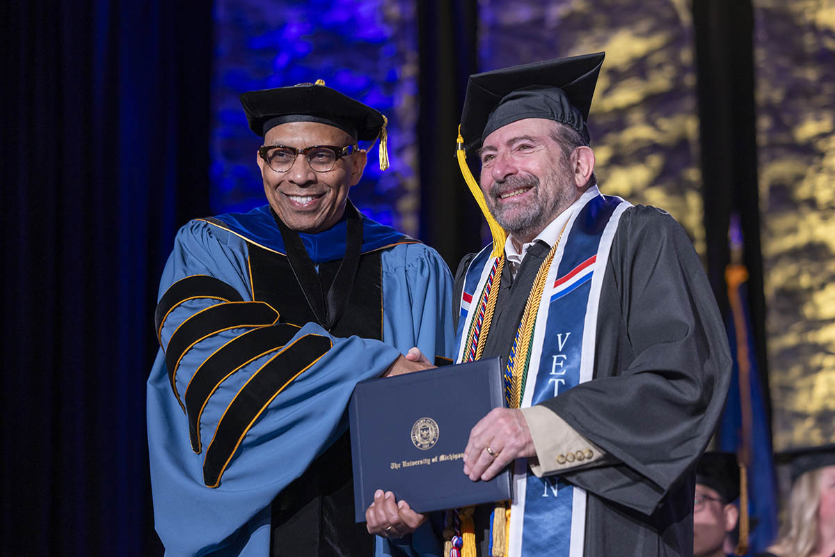 A student receiving his diploma on stage from Chancellor Laurence Alexander.
