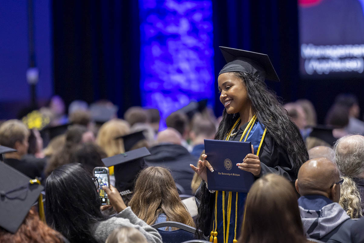 A student standing in the crowd posing with her diploma cover for the camera