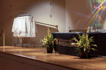 An empty stage at the physician assistant white coat ceremony showcasing a rack of white coats waiting to be distributed.