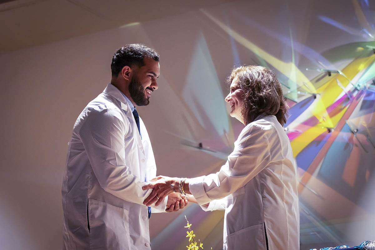 A student shaking hands with a faculty member after receiving his white coat.