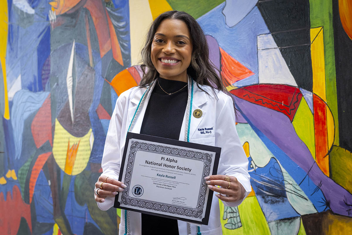 A student with her white coat holding up a certificate that is titled "Pi Alpha National Honor Society."