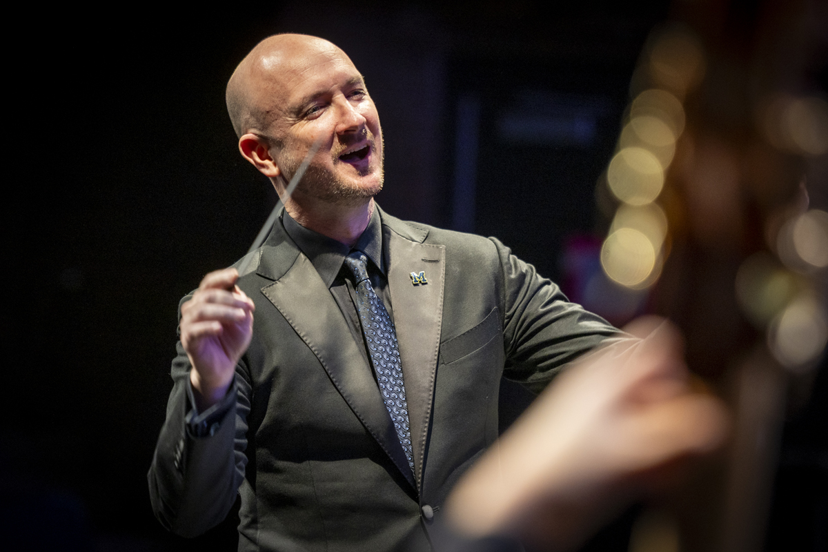 Conductor in mid-motion, leading with a baton and a smile.