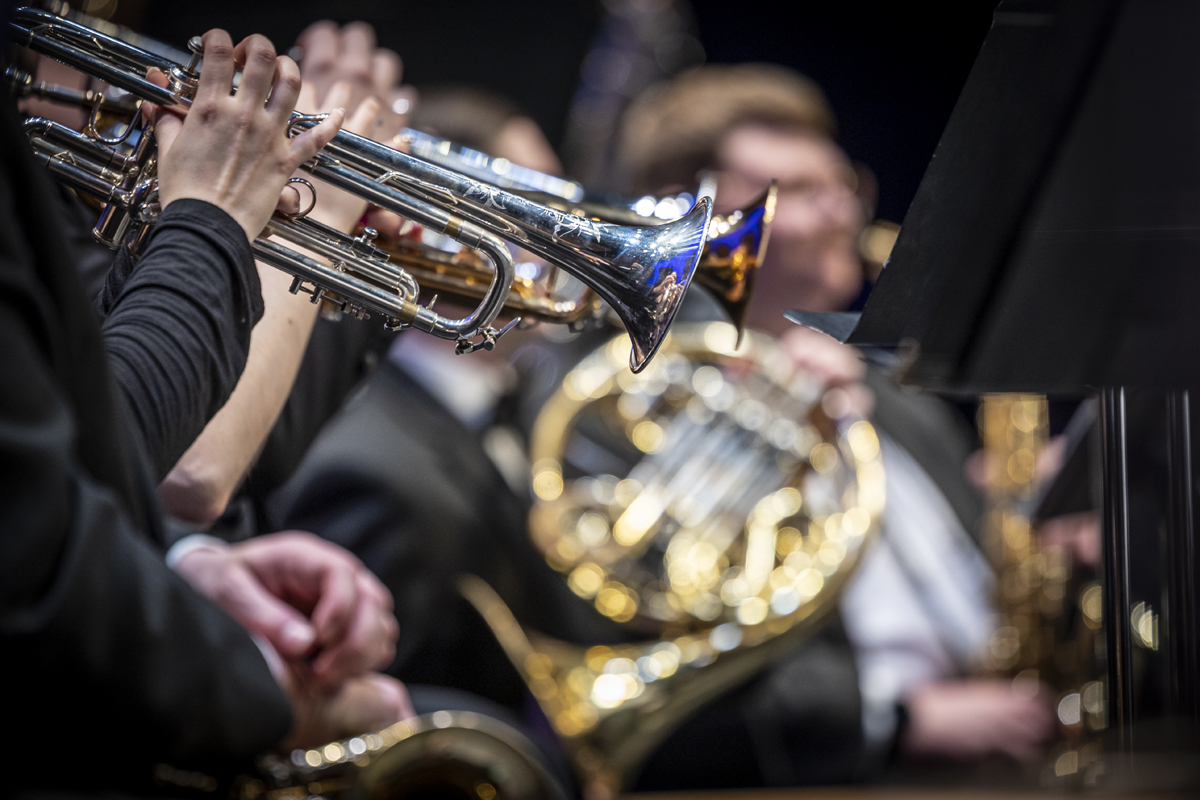 A tight shot of trumpet and French horn players mid-performance, focusing on the gleaming brass instruments and players' hands in motion.