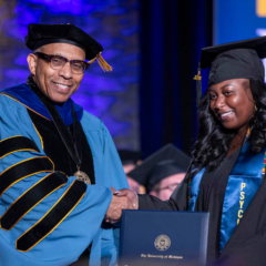 A student receiving her diploma on stage from Chancellor Laurence Alexander